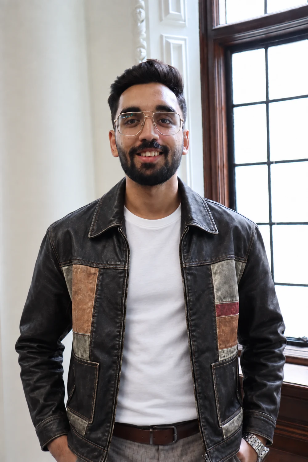Keshav standing beside a window in a dark jacket